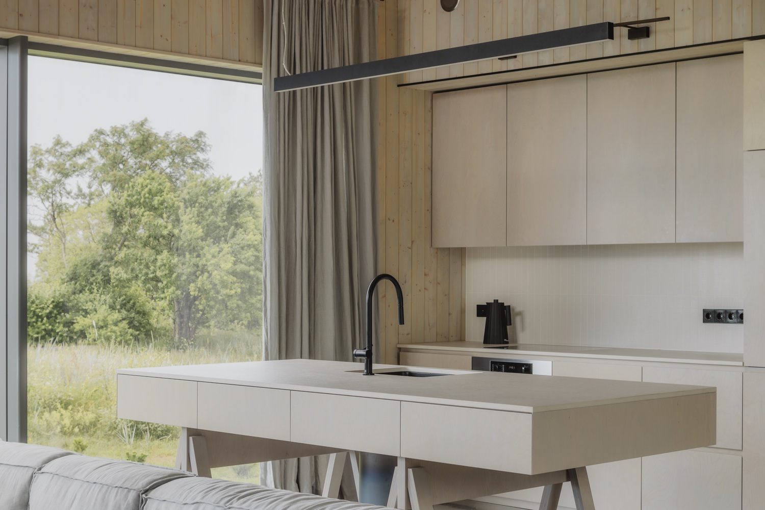 Open kitchen with white island and timber ceiling overlooking green landscape through floor-to-ceiling glazing
