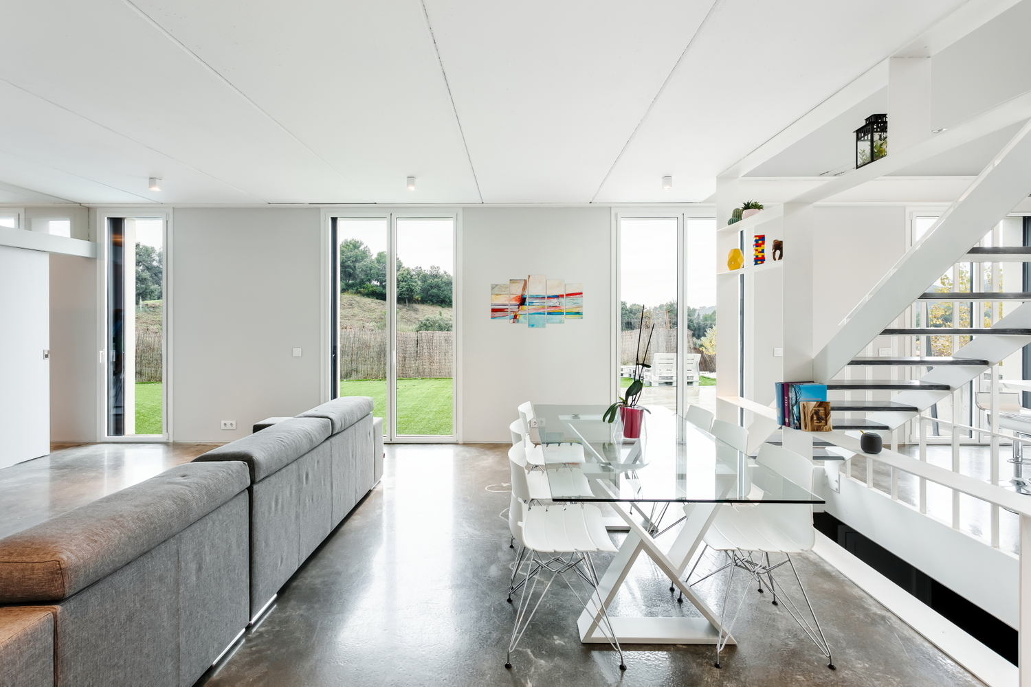 Open living and dining space with polished concrete floors and floor-to-ceiling glazing overlooking a garden