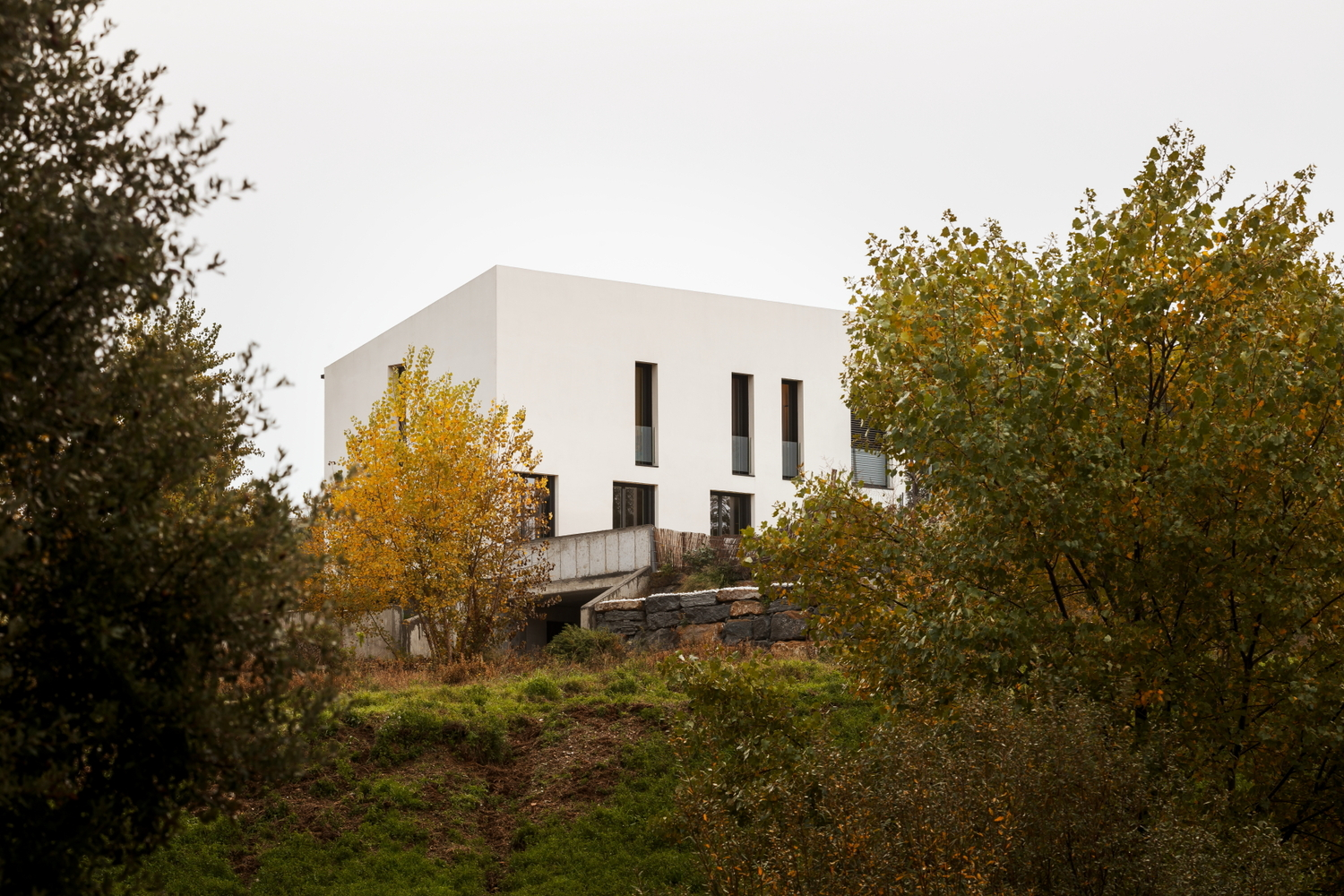 White cubic volume on a hillside surrounded by trees with autumn foliage