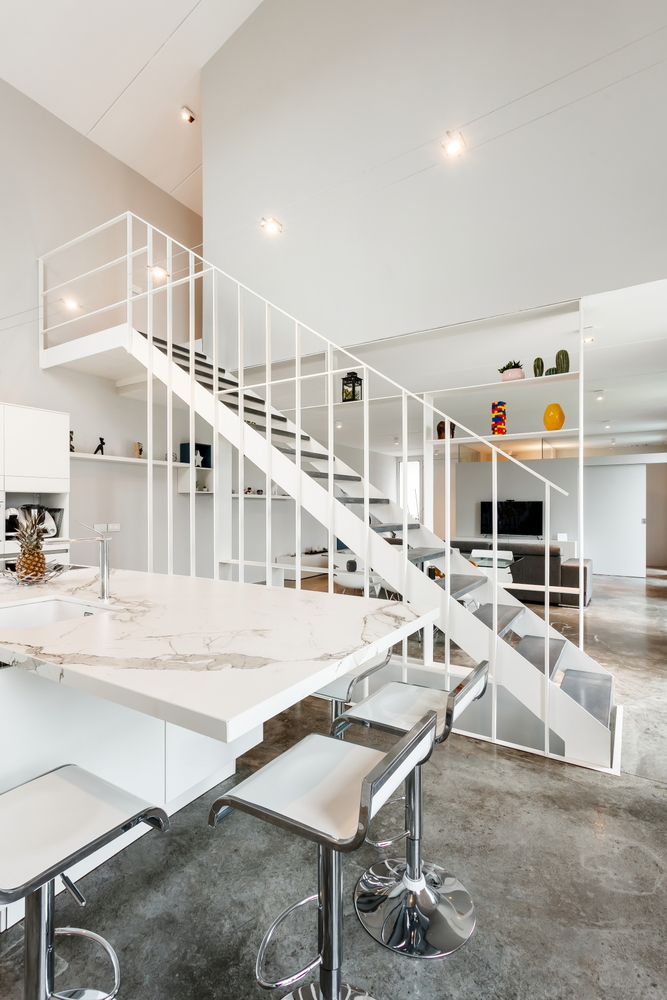 White steel staircase ascending beside a marble kitchen island under pendant lights