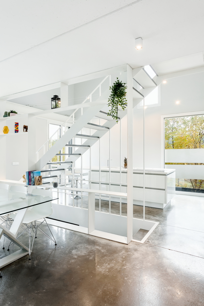Double-height interior with white steel stair and railing framing a view to the window and autumn trees