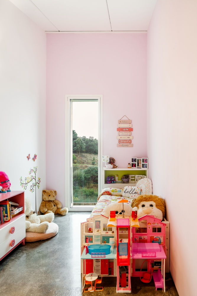 Pink-painted bedroom with floor-to-ceiling window overlooking green landscape and scattered toys