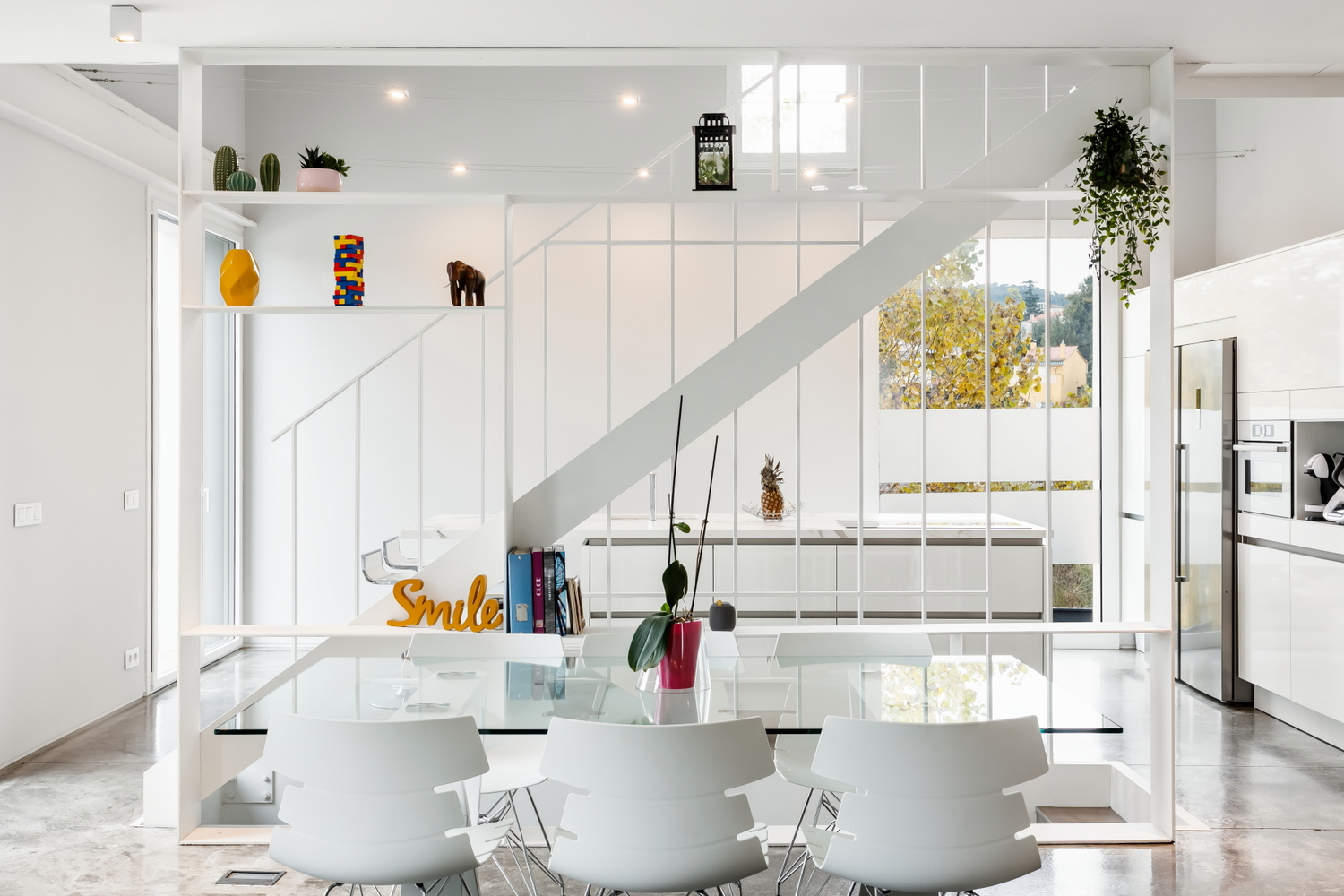 Dining table framed by the white steel stair structure with hanging plants and distant view of trees