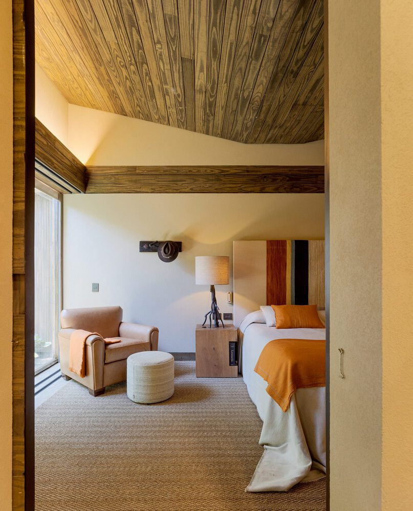 Bedroom view through doorway showing wood-lined vaulted ceiling and bed with ochre throw
