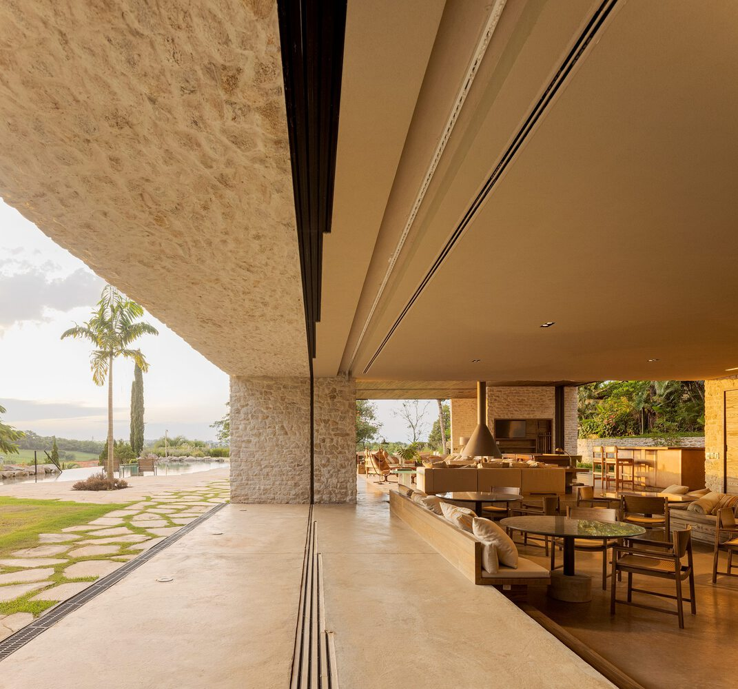Open-air terrace with limestone columns and sliding glass doors overlooking lawn and palm tree