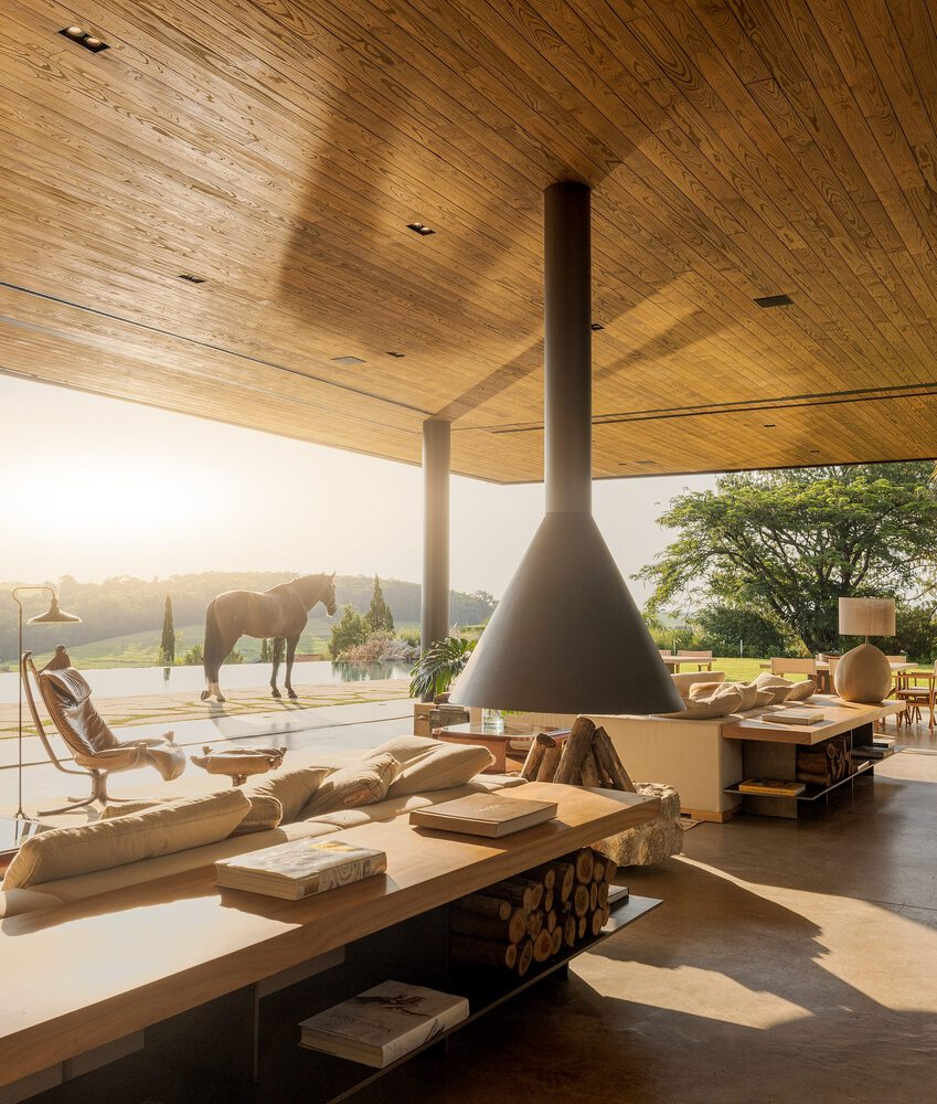 Open-air living room with a suspended conical fireplace and horse standing on the terrace beyond