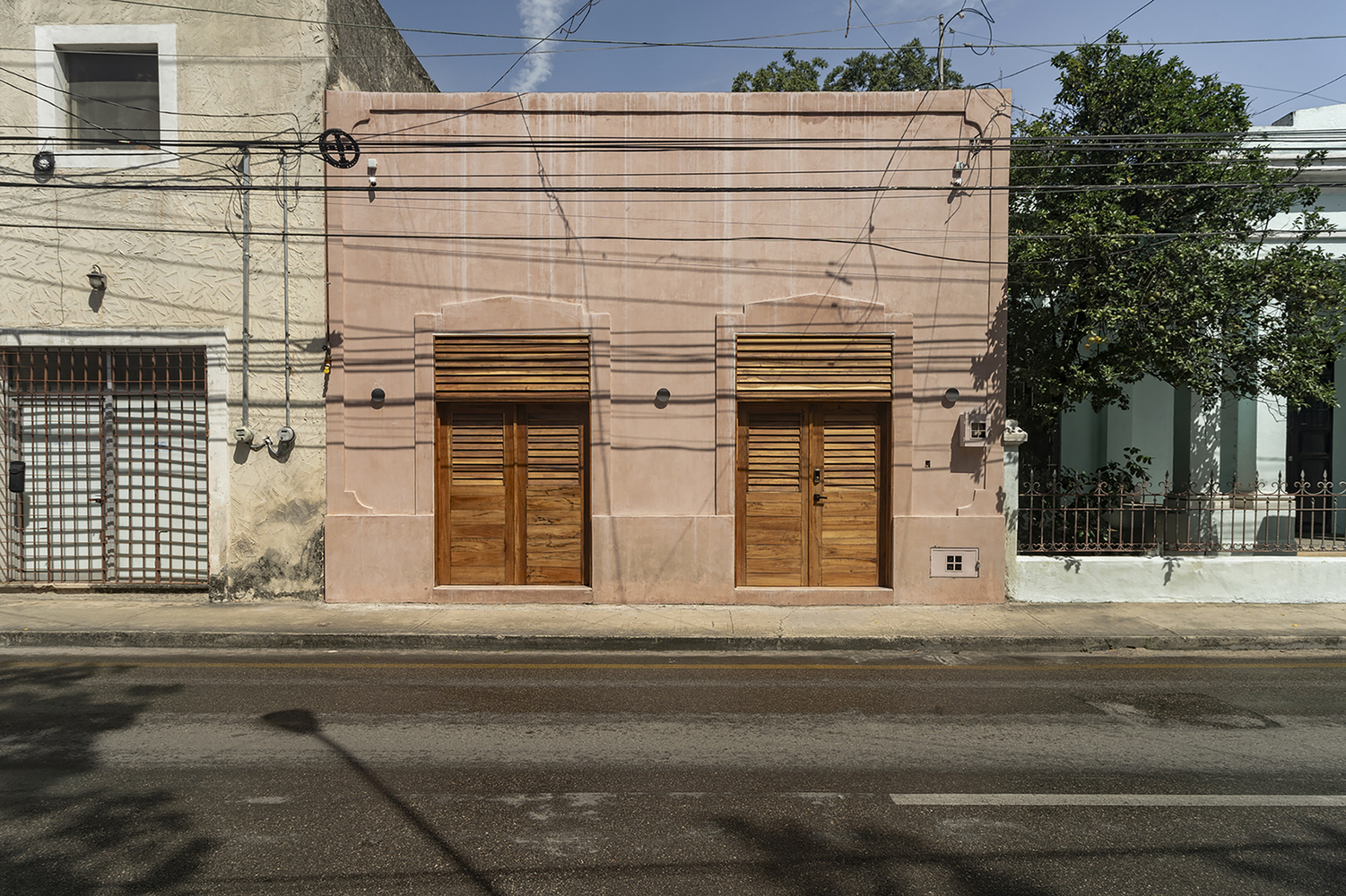 Street view of a pink stucco facade with two timber louvered doors beneath overhead power lines