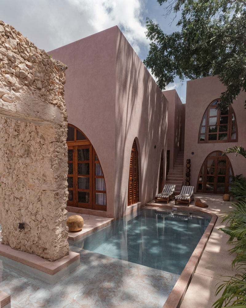 Courtyard pool framed by pink stucco walls and arched timber doors beside a weathered stone wall