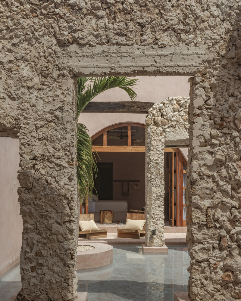 View through a ruined stone archway to an interior courtyard with palms and arched timber windows