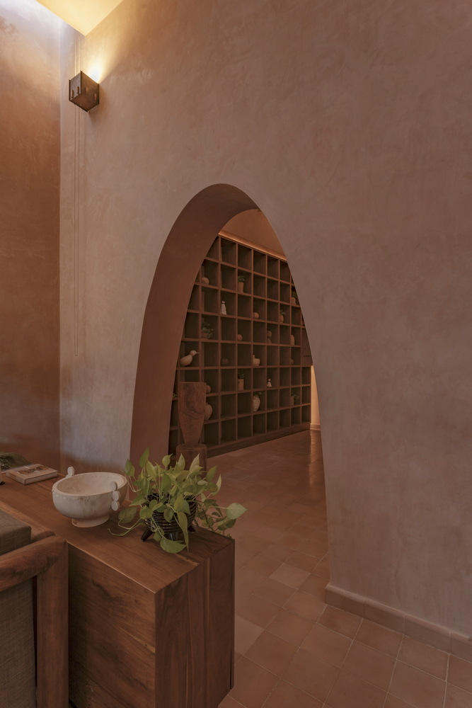 Interior arched niche with timber gridded shelving set into a pink plastered wall at dusk