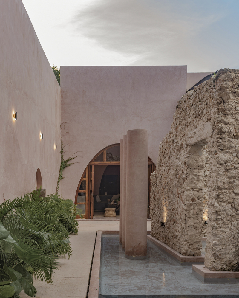 Courtyard at dusk with a narrow lap pool running between pink walls and a stone ruin