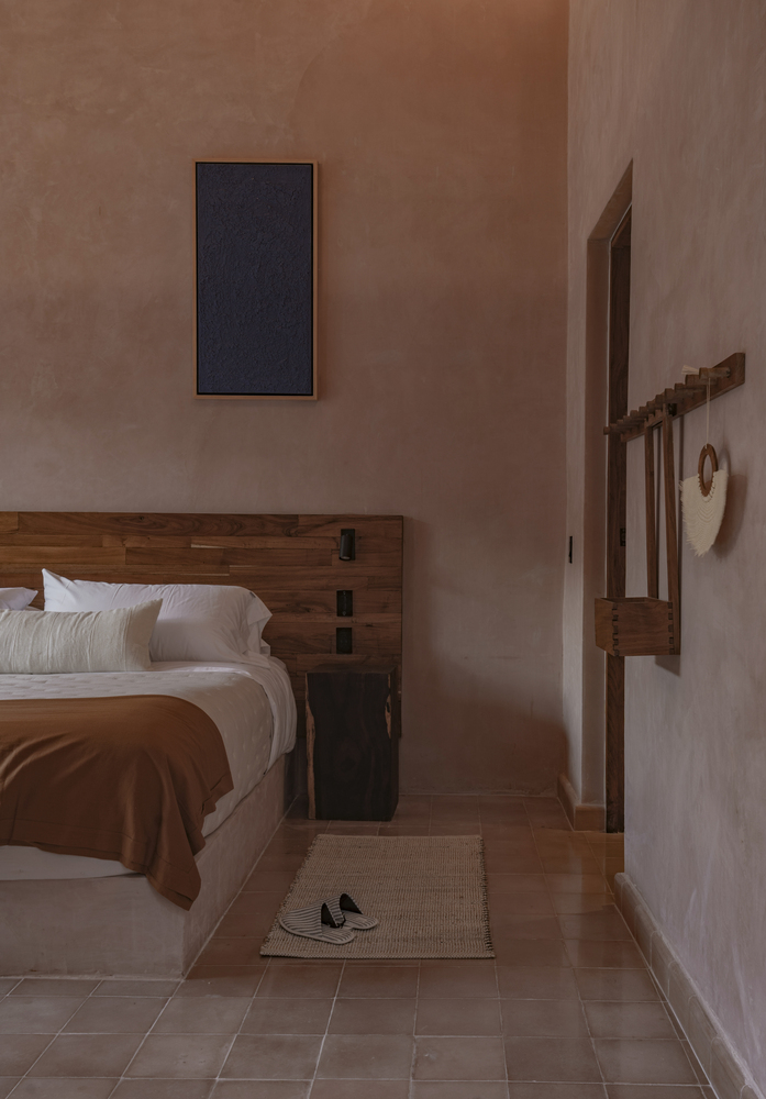 Bedroom with timber-framed bed and earthen plaster walls in warm afternoon light