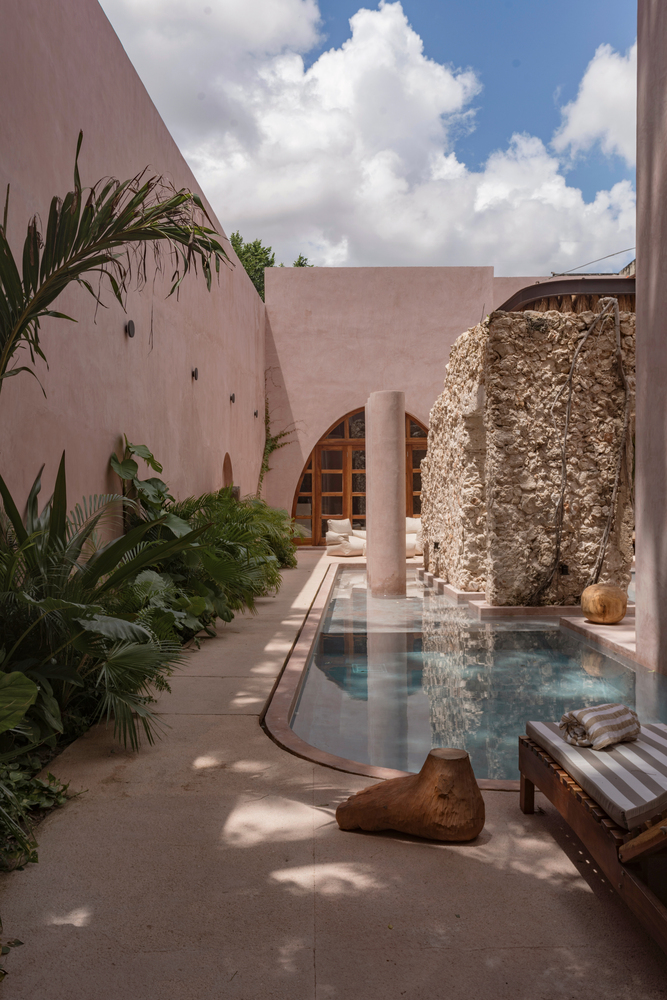 Courtyard pool surrounded by pink stucco walls and preserved stone ruins under white clouds
