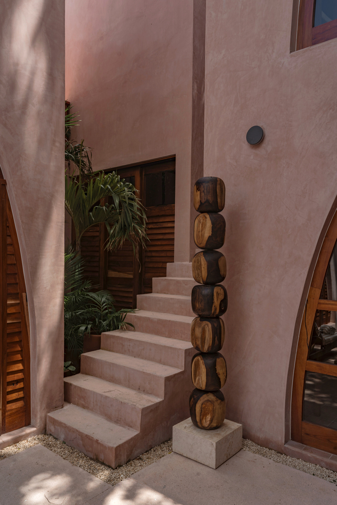 Exterior staircase with stacked timber sculpture beside potted plants at dusk