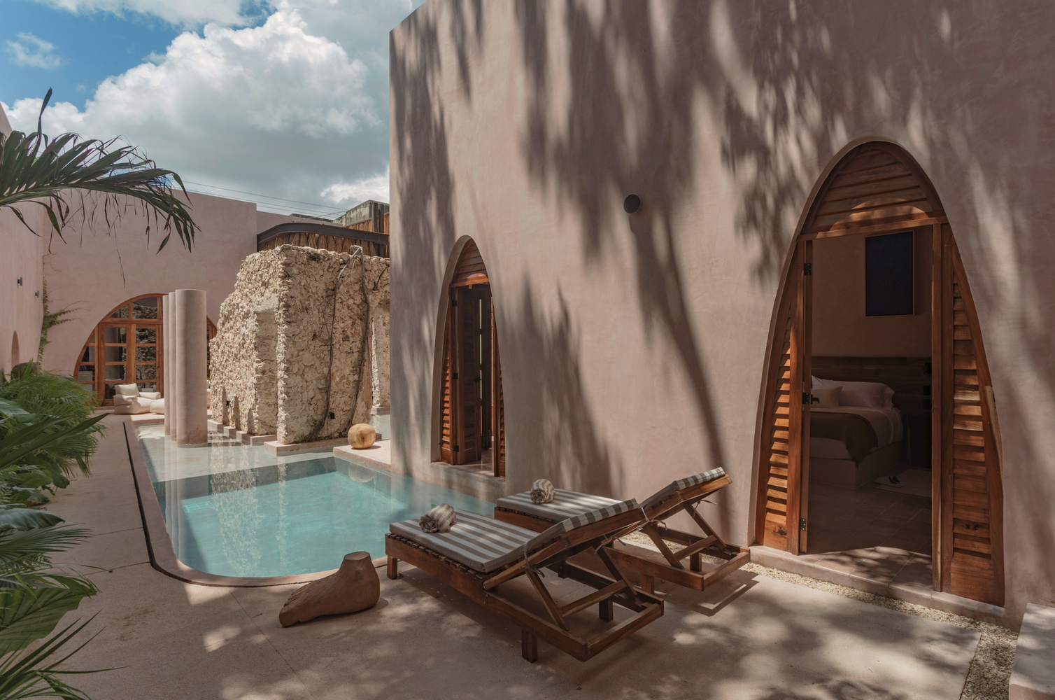 Poolside terrace with arched timber doors and dappled palm shadows on pink walls