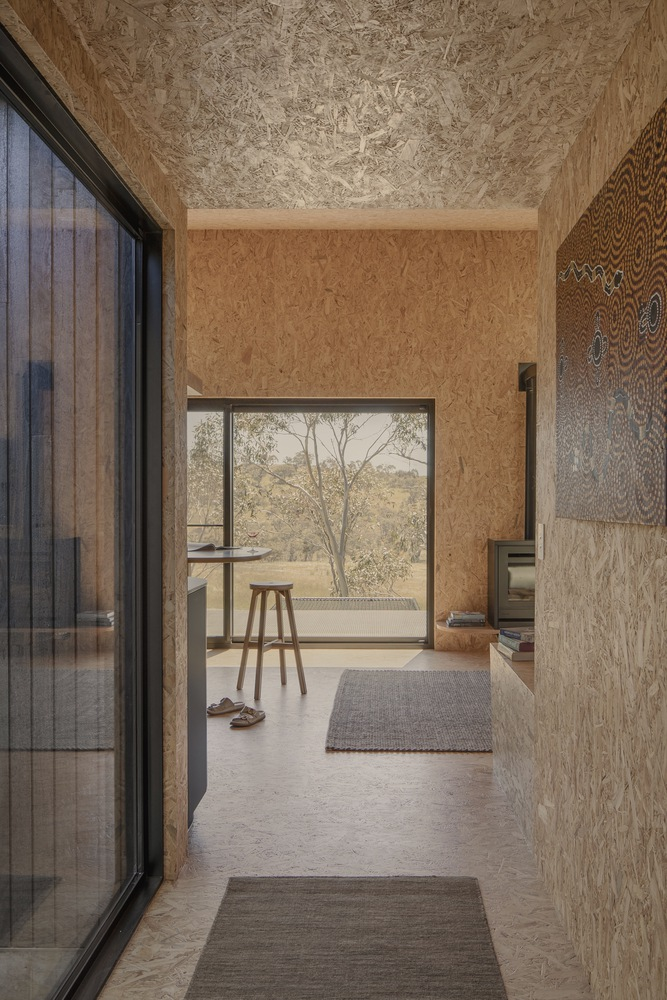 Hallway view through oriented strand board walls toward a picture window overlooking distant eucalyptus trees