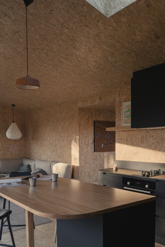 Kitchen and dining area with oriented strand board surfaces lit by afternoon sunlight through adjacent windows