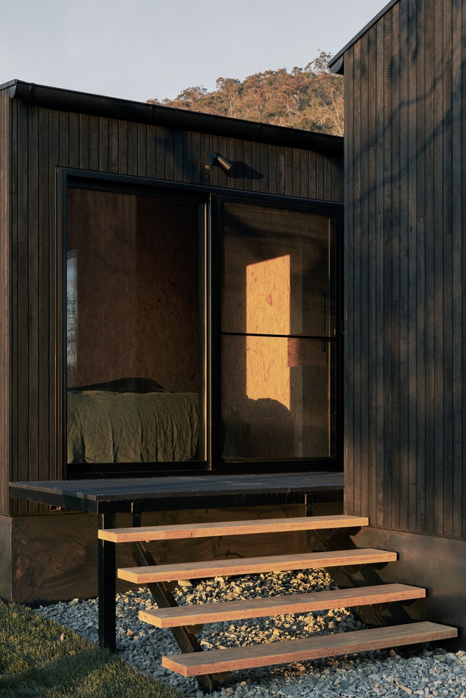 Exterior timber steps leading to glazed bedroom opening at dusk with warm interior light