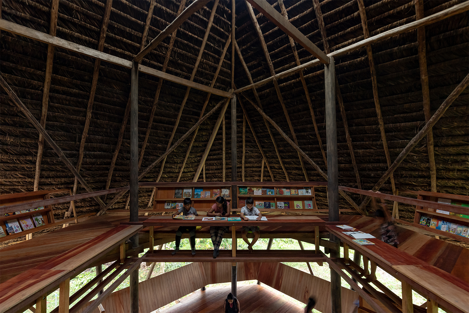 Interior view of the steep thatched roof structure with diagonal timber bracing above tiered reading desks