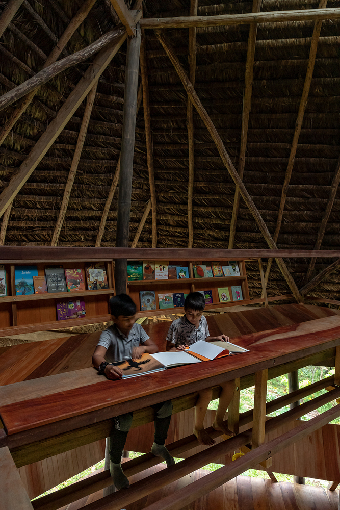 Upper reading level with timber desk and book display under the exposed thatch and bamboo rafters