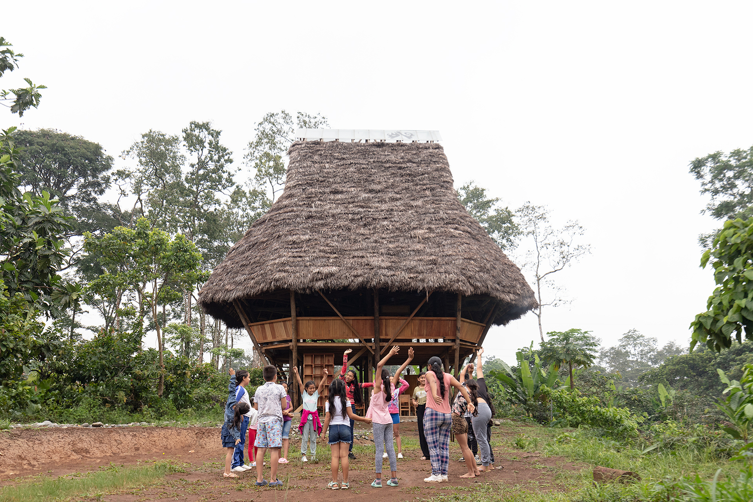 Thatched roof pavilion elevated on timber columns with a group of children gathered below