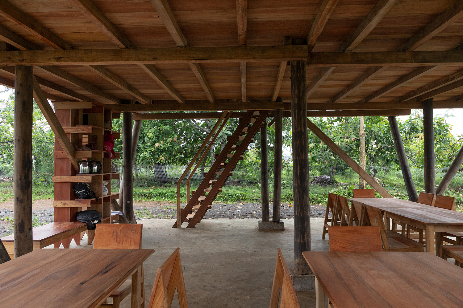 Open-air ground floor with exposed timber frame, diagonal bracing, and wooden benches beneath a coffered ceiling