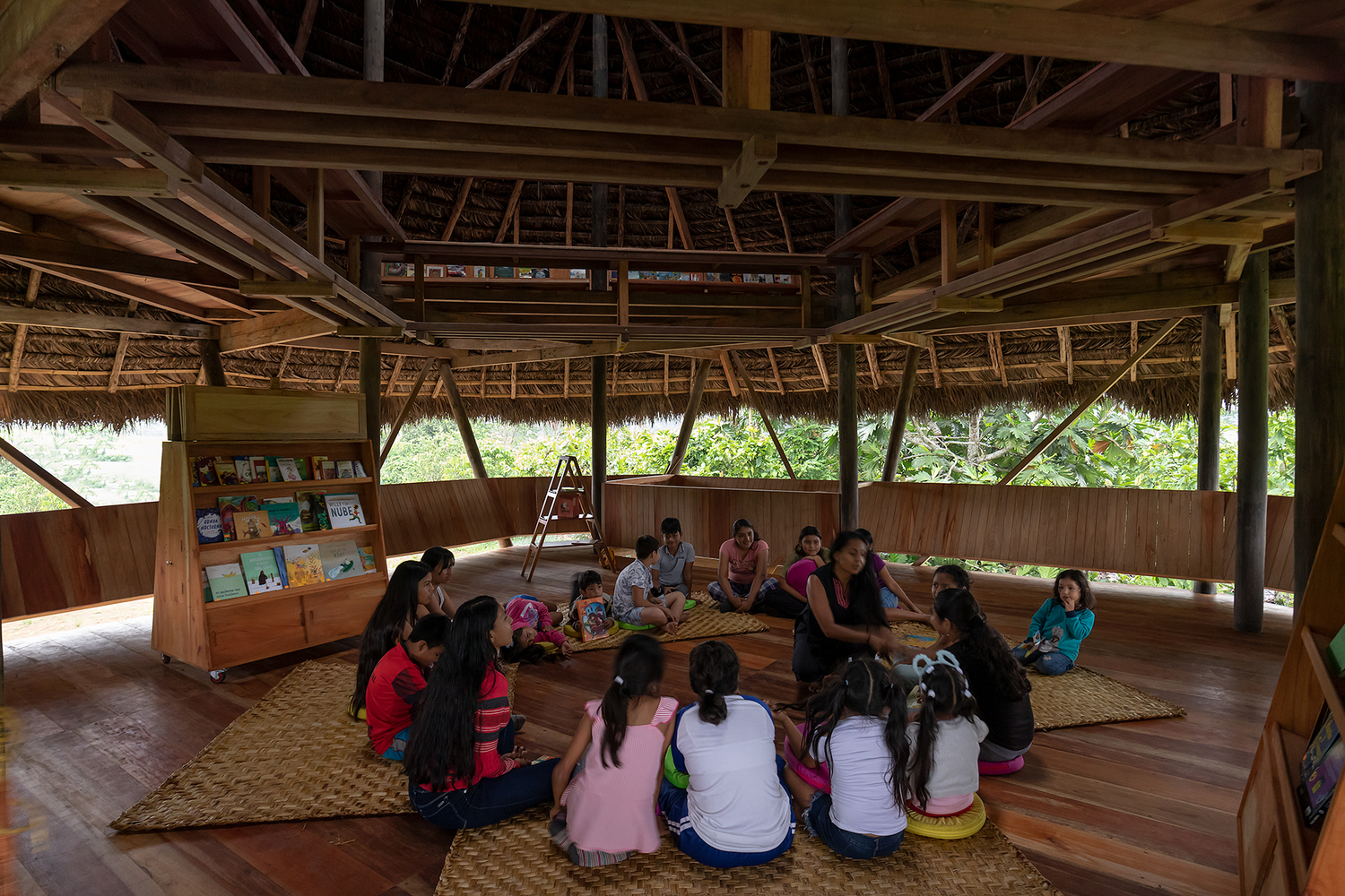 Upper floor interior with timber framing and thatched roof where children sit in a circle on mats
