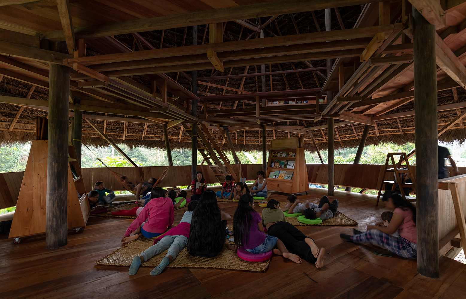 Interior view showing the exposed timber truss structure and children reading on floor mats