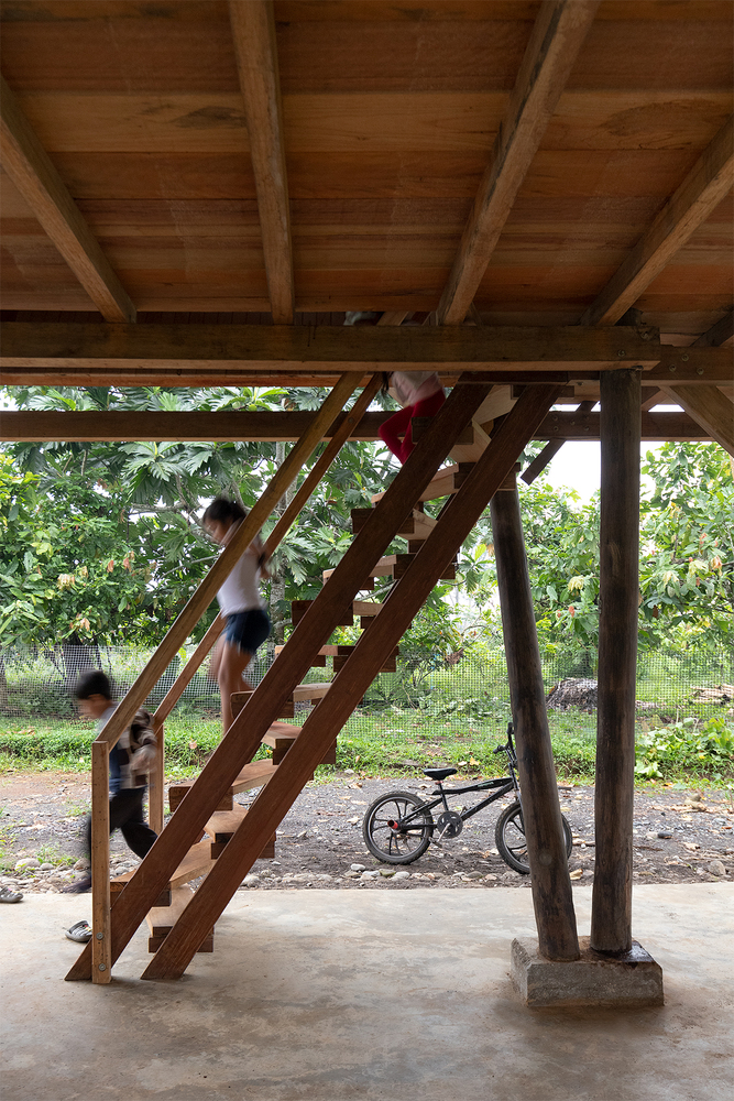 Steep timber staircase beneath an exposed wood ceiling with children playing and a bicycle parked below