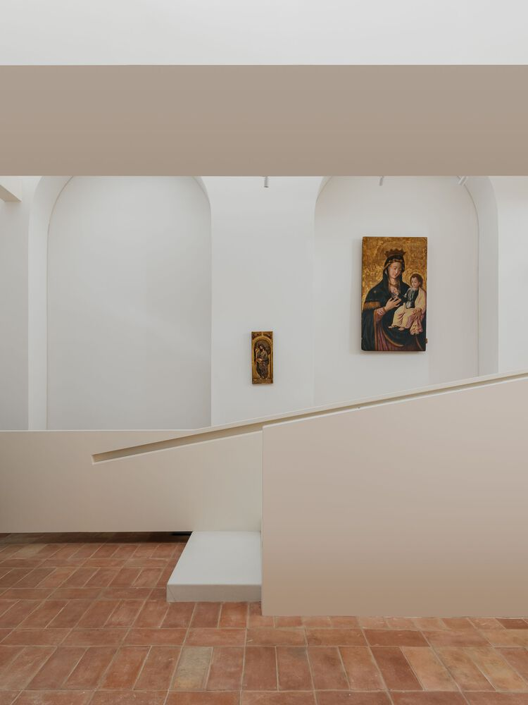Curved white balustrade overlooking gallery space with religious paintings mounted in arched alcoves