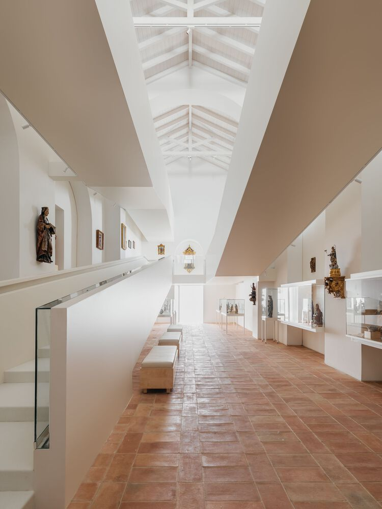 Upper gallery corridor with exposed white timber roof trusses and terracotta tile floor stretching into distance