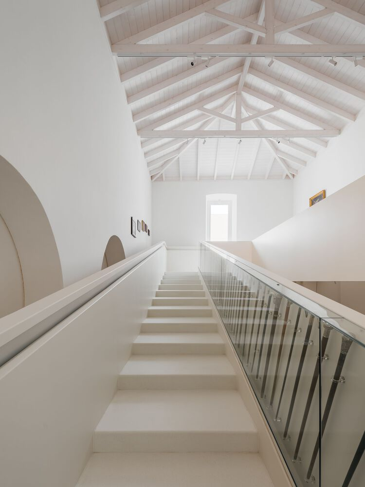 Staircase rising toward exposed timber roof structure with central skylight above white plastered walls