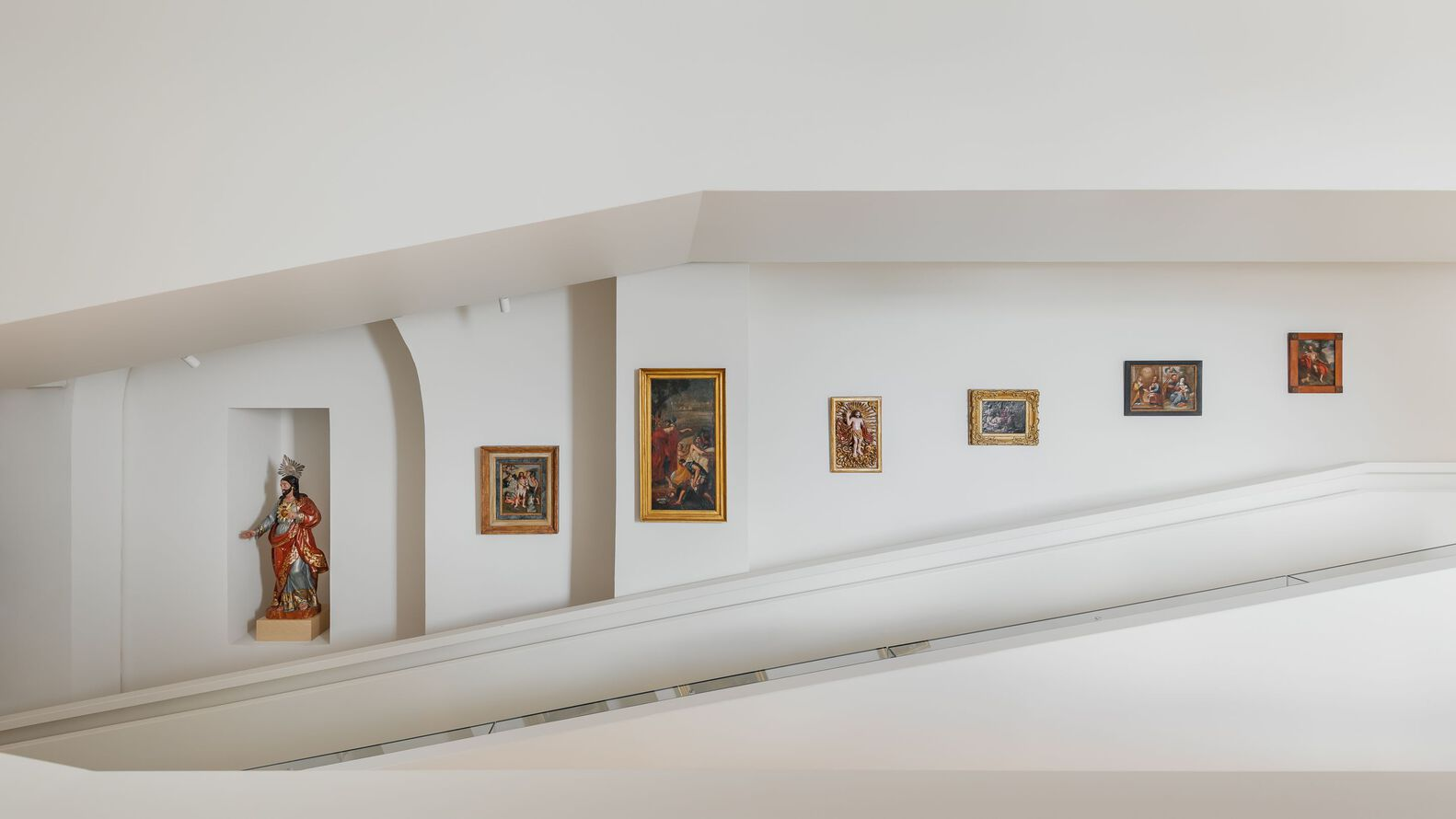 Upper gallery level with sculpture in arched niche and framed paintings along white parapet wall