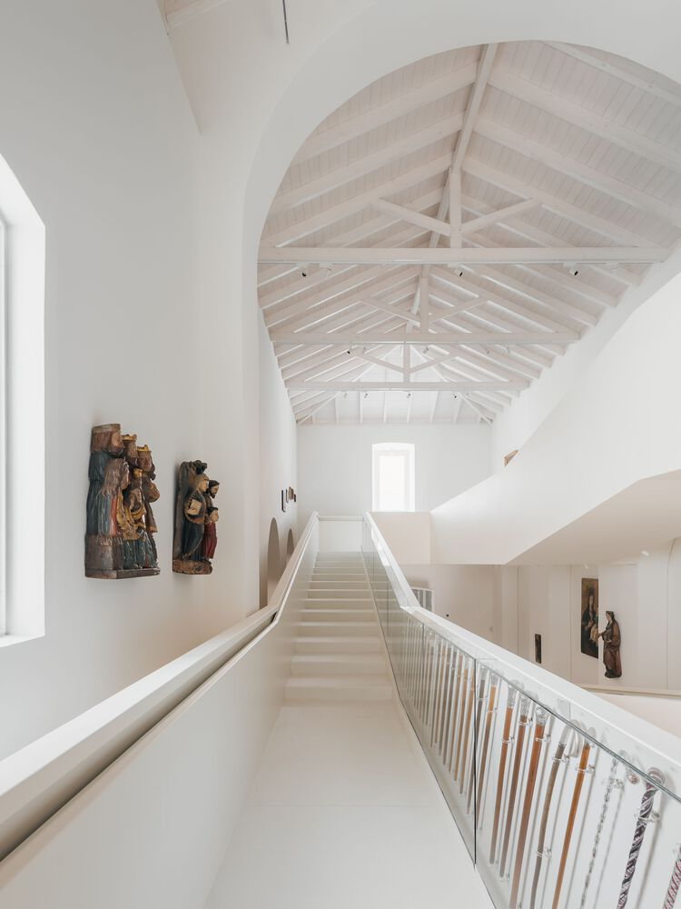 Bridge walkway with metal railing spanning between upper gallery levels beneath exposed timber truss ceiling