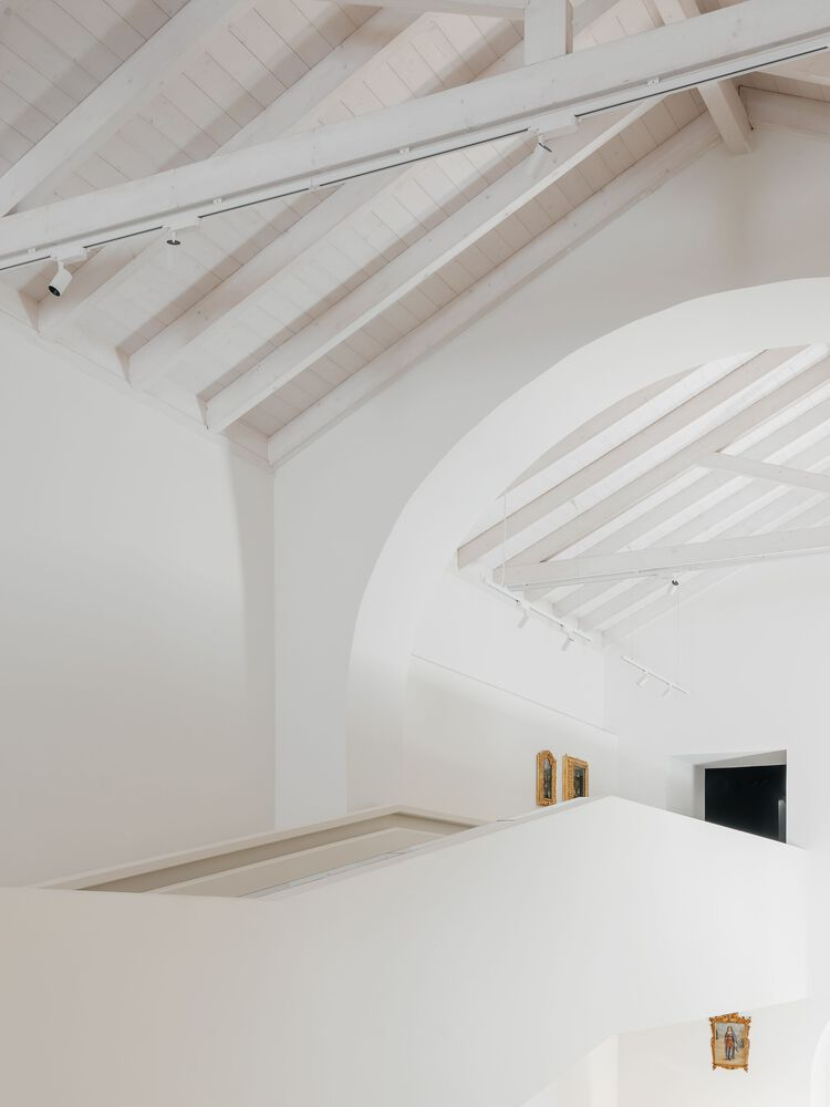 Detail of intersecting white barrel vaults with exposed timber roof rafters and track lighting mounted above