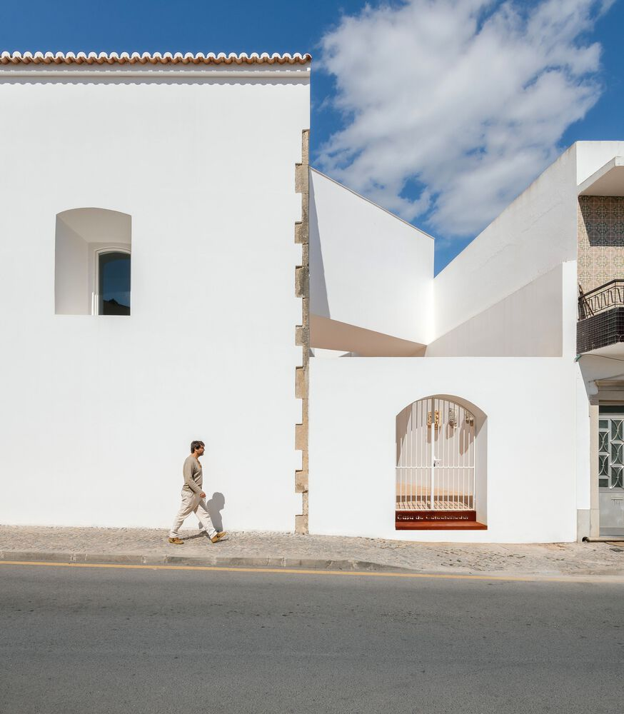 Street facade with arched openings and cantilevered volume as a pedestrian walks past in daylight