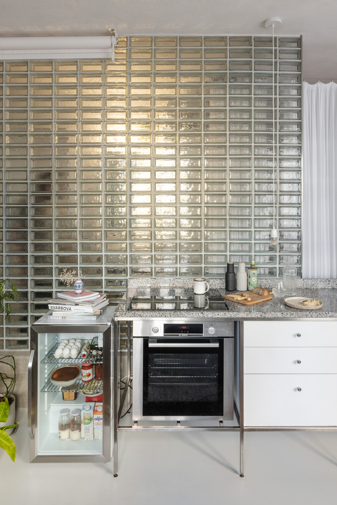 Kitchen counter with oven and mini fridge below a full-height glass block wall glowing with daylight