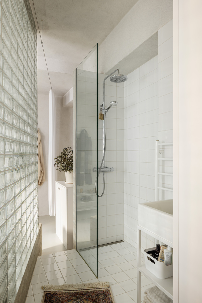 Bathroom with glass shower enclosure and white tile walls next to a translucent glass block partition