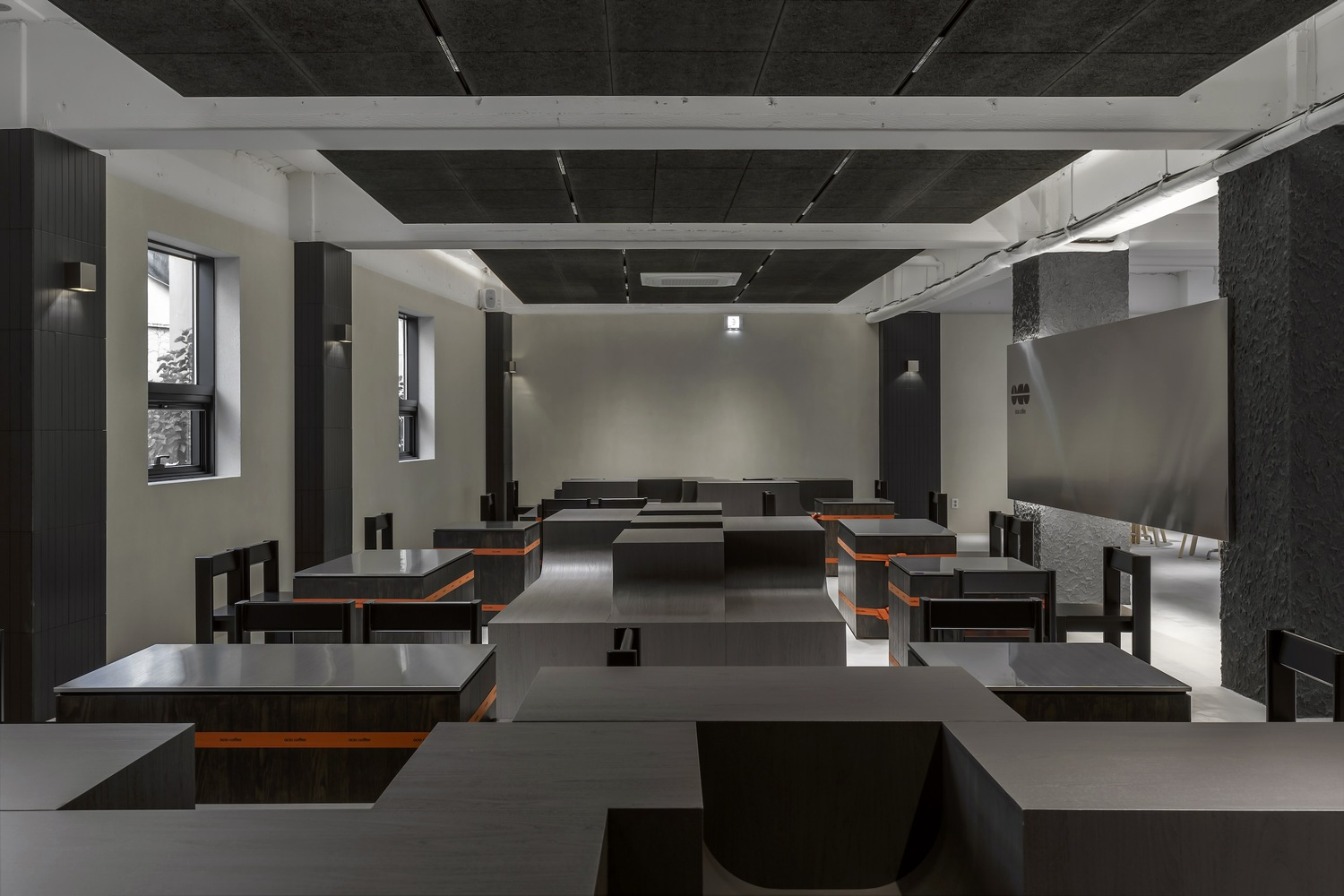 Interior dining hall with rows of black tables and benches under exposed concrete beams and dark ceiling panels