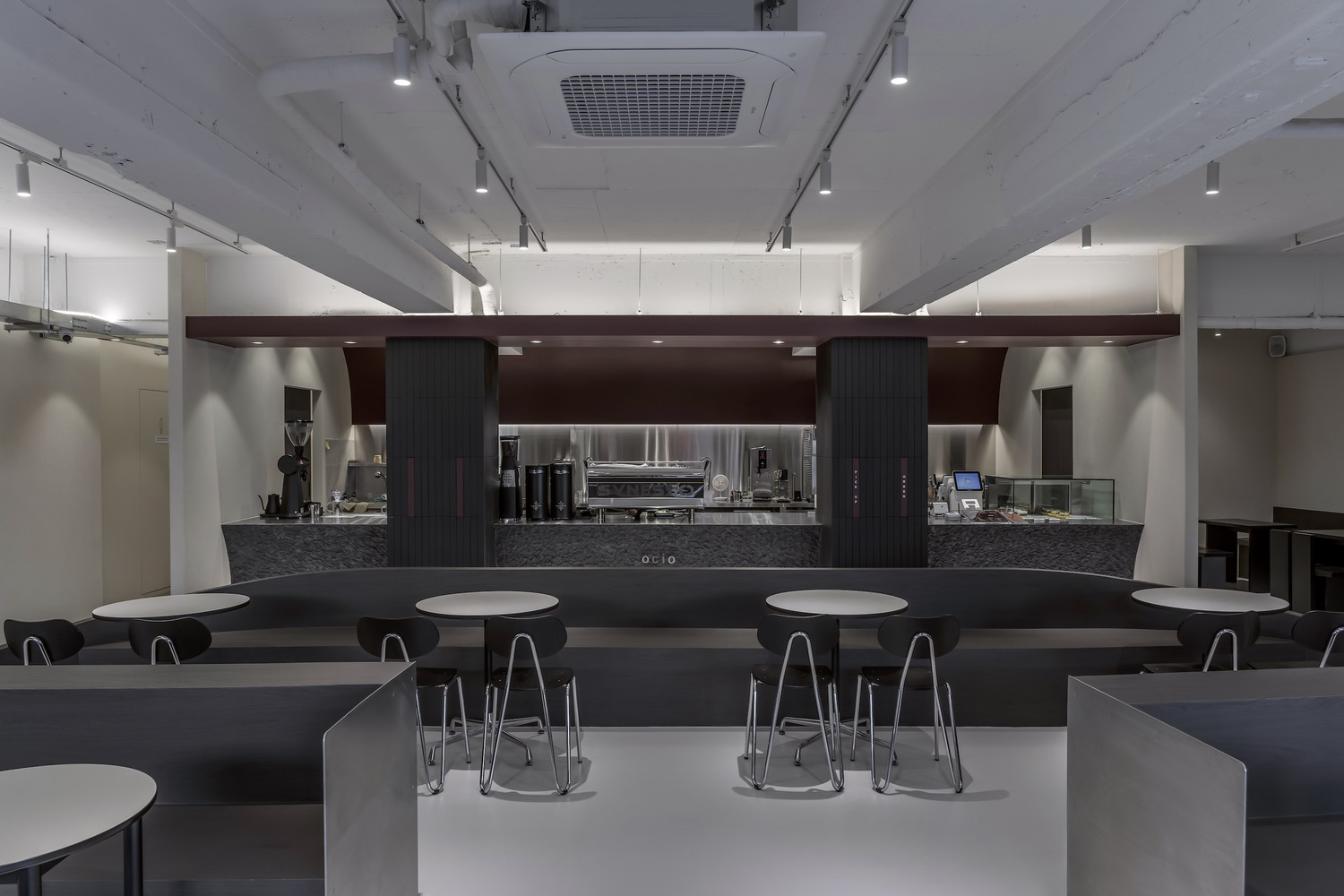 Service counter with stainless steel and dark wood cladding backed by open kitchen equipment in bright light