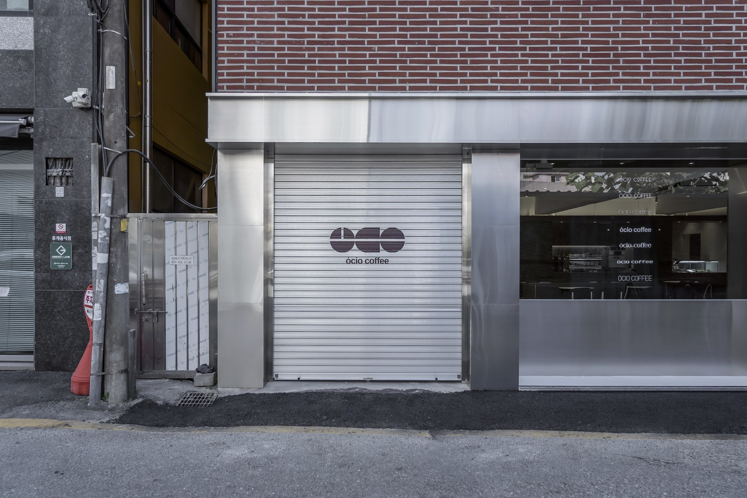 Storefront entrance with metal roll-down shutter beside glass window and red brick facade above white band
