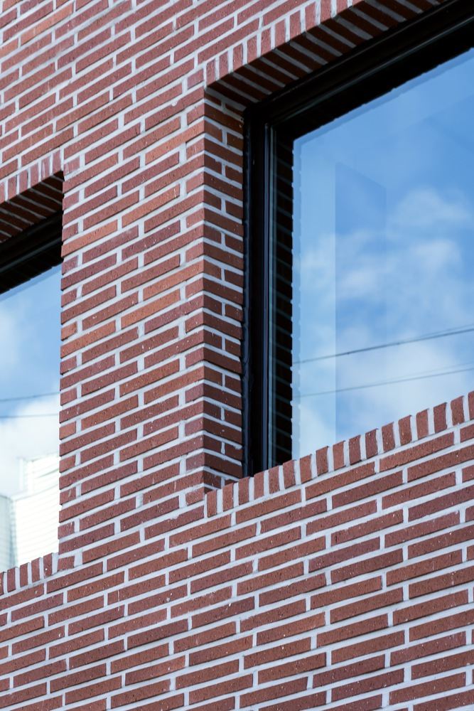 Corner detail of red brick wall meeting black metal window frame with clouds reflected in glass