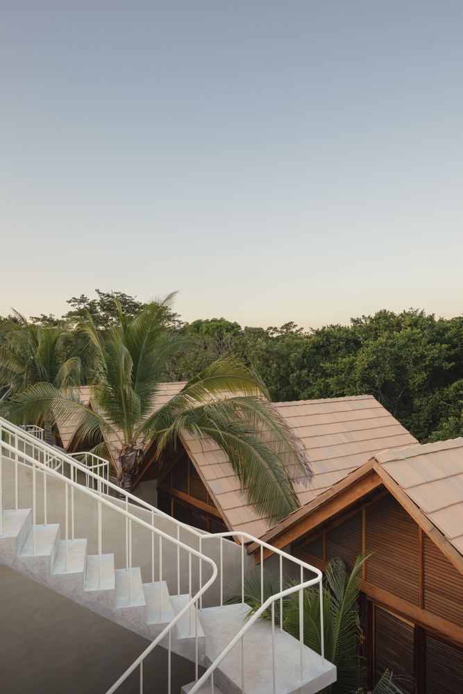 White curved staircase descending from a rooftop terrace past palm trees and pitched timber roofs at dusk
