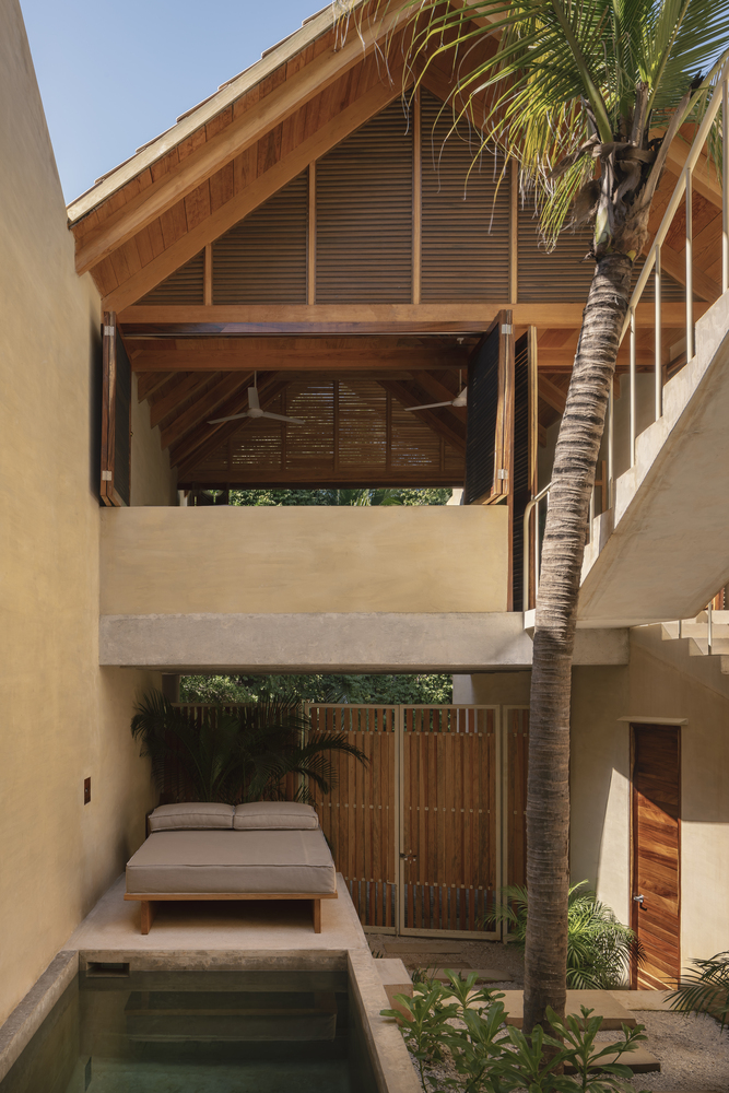 Private courtyard with plunge pool and daybed beneath a gabled balcony framed by a palm tree