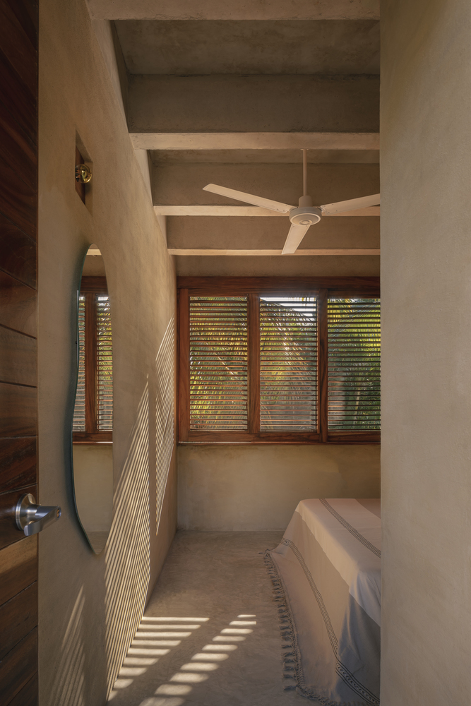 Bedroom with exposed concrete beam ceiling and timber louvered windows filtering afternoon sunlight across floor