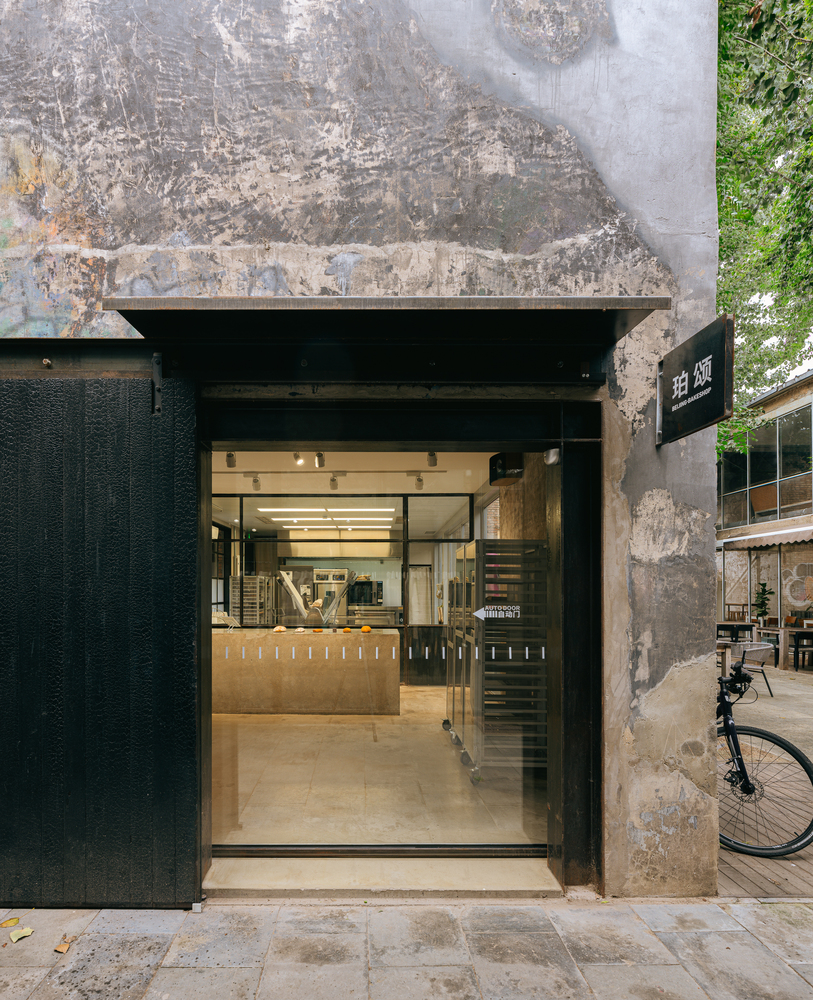 Narrow entrance with charred timber cladding set into a weathered concrete wall