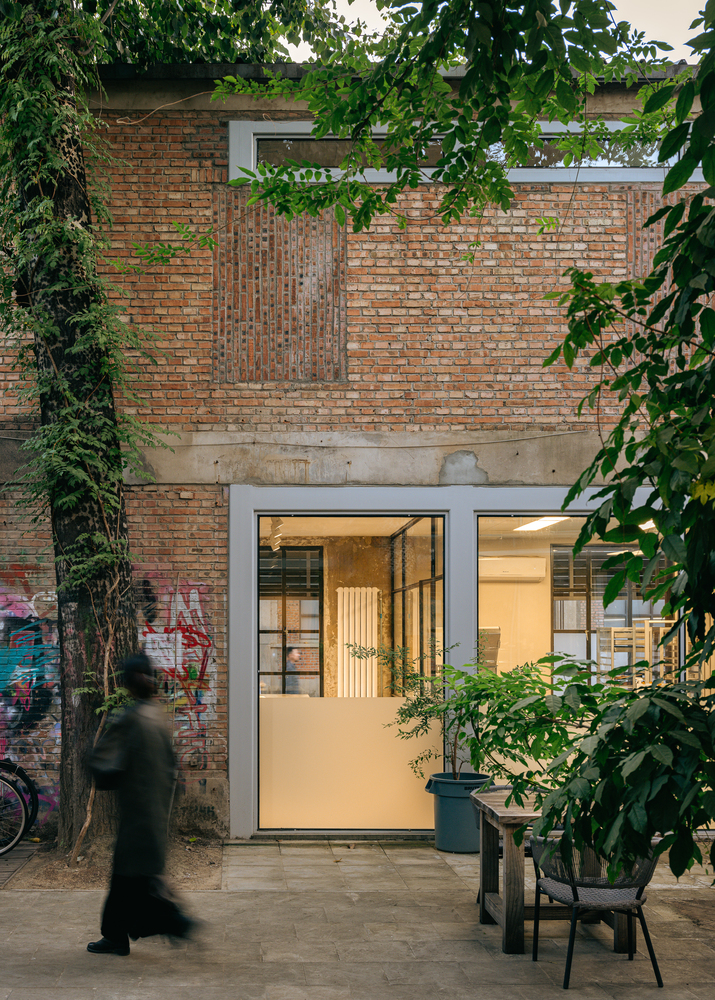 Glazed entrance set within weathered brick wall framed by climbing ivy and green foliage