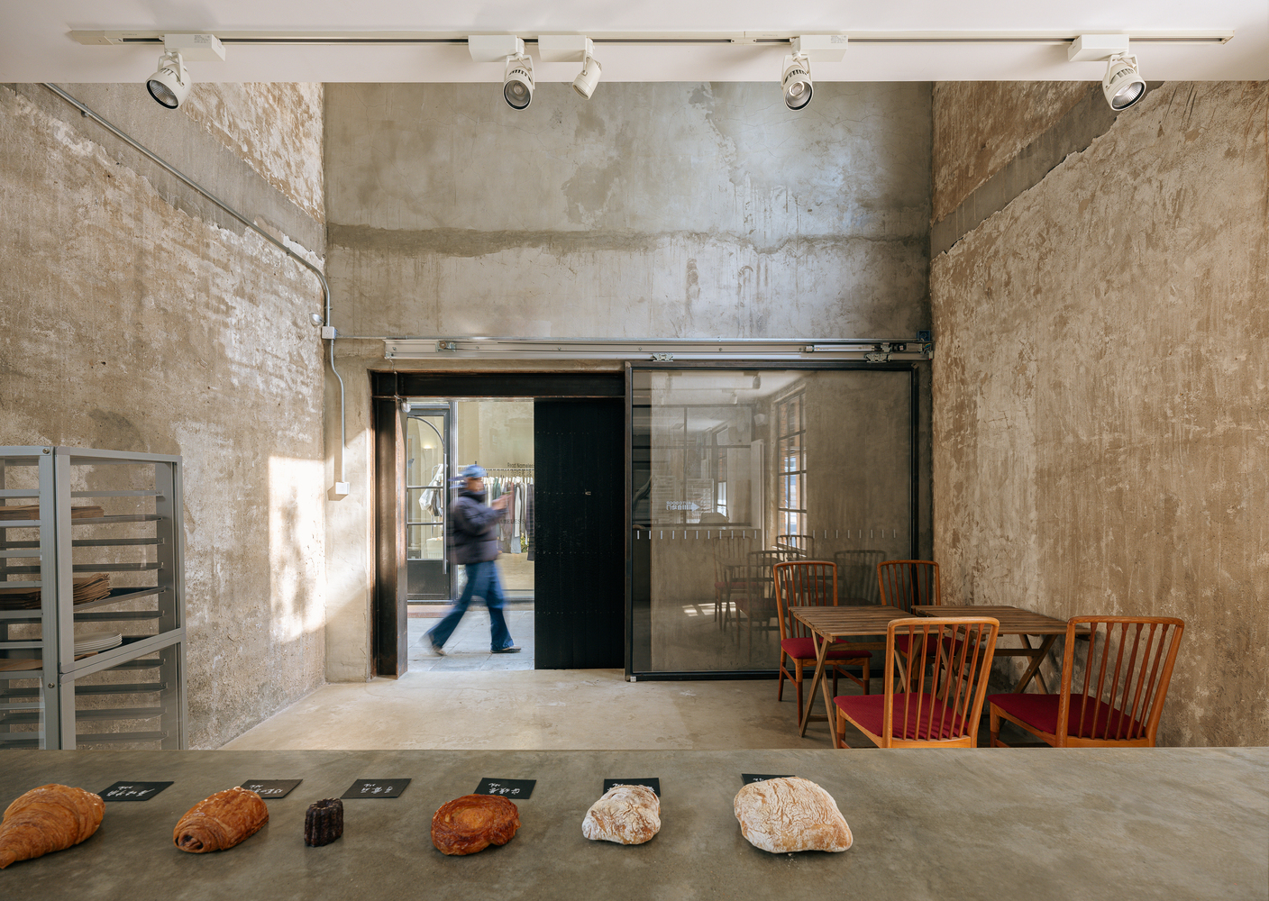 Interior view with concrete walls and sliding glass partition looking toward figure walking through doorway