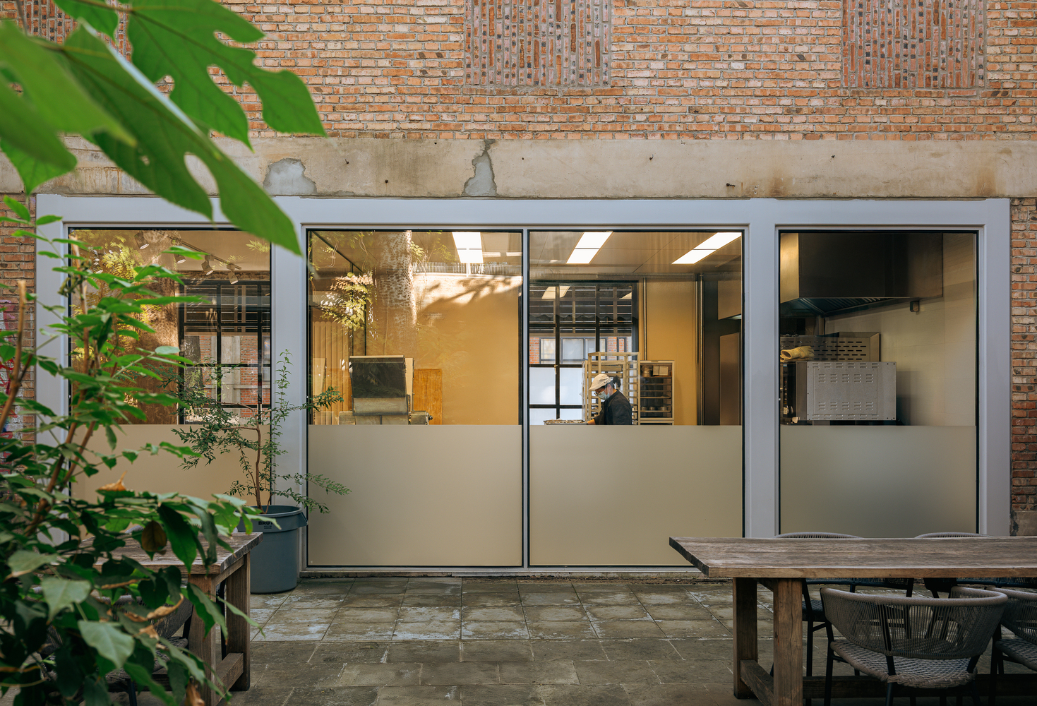 Courtyard view of frosted glass sliding doors beneath concrete lintel and brick facade with potted plants