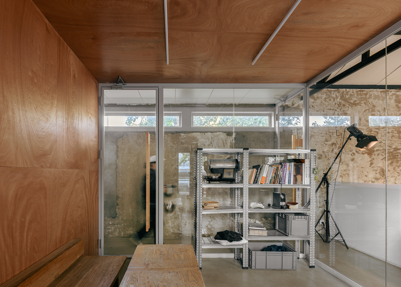 Plywood-clad room with metal shelving unit and glazed partitions revealing aged concrete walls beyond